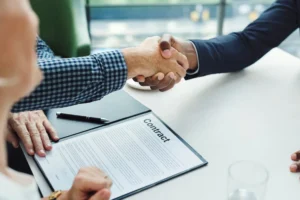 Dos hombres estrechando la mano frente a un contrato